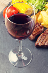 Red wine glass and steak with grilled potato, corn, salad