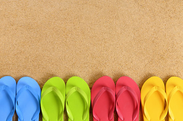 Fototapeta na wymiar Row line of several pairs colorful flip flop sandals on a sand beach background lower border space for copy text photo