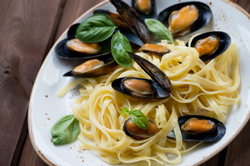 Boiled mussels with tagliatelle and basil on a plate, close-up