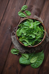 Fresh spinach leaves in a wooden bowl over dark wooden surface © Nickola_Che