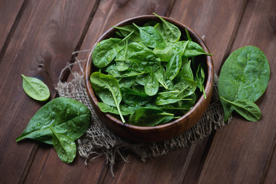 Fresh spinach leaves over dark brown wooden background