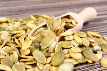 Pumpkin seeds with spoon on wooden background