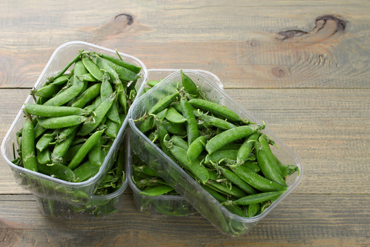 fresh green peas in a plastic container on a wooden background