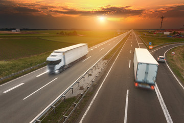 Two white trucks in motion blur on the highway at sunset
