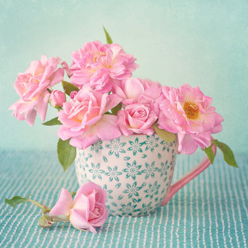 Beautiful fresh roses in a porcelain cup on a green background .