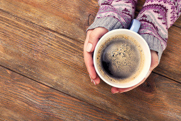 Female hands holding cup of coffee on wooden background