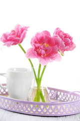 Pink tulips in glass vase with cup on tray, isolated on white
