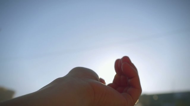 Woman's hand catching sunlight and sun against clear blue sky