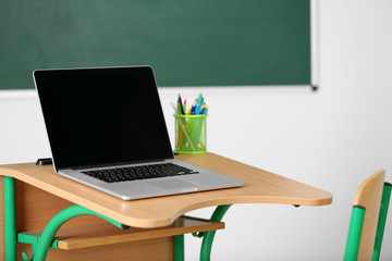 Naklejka premium Wooden desk with stationery and laptop in class on blackboard background
