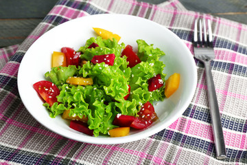 Bowl of fresh green salad on table with napkin, closeup