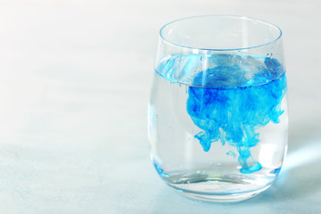 Glass of water with blue paint on table close up