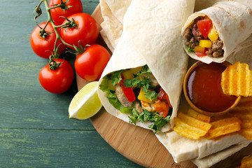 Homemade tasty burrito with vegetables, potato chips on cutting board, on wooden background