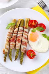 Dish of asparagus with bacon and egg in plate on table, closeup