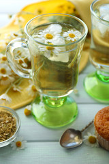 Glass of chamomile tea with chamomile flowers and tasty muffins on color wooden background
