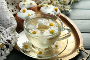 Cup of chamomile tea with chamomile flowers and tasty muffins on tray, on color wooden background