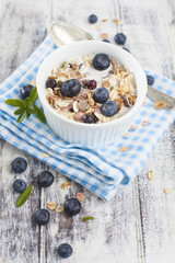 Bowl of muesli with fresh blueberries and glass of yogurt on whi