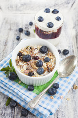 Bowl of muesli with fresh blueberries and glass of yogurt on whi