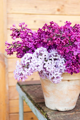Ceramic pot with a branch of lilac flower on wooden background