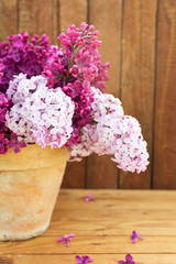 Ceramic pot with a branch of lilac flower on wooden background