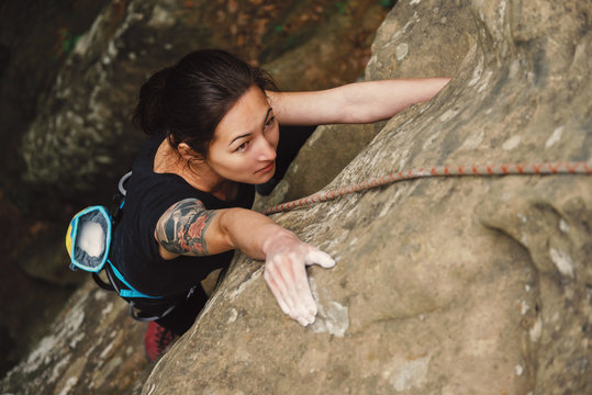 Beautiful young woman climbing on rock