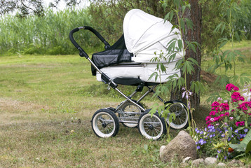 Modern white pram standing outdoors under the tree