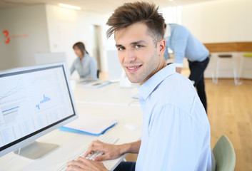 Fototapeta premium Office worker sitting in front of desktop, colleagues in background