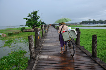Old man bring bicycle cross over lake at U Bein Bridge