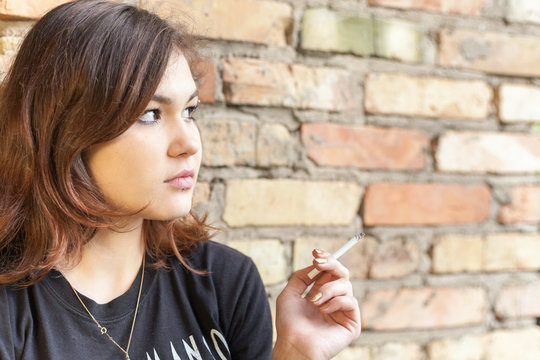 Schoolgirl teenager smokes outdoor on brick wall background