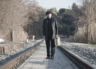 HOMBRE ELEGANTE JUNTO A LAS VIAS DEL TREN CON SOMBRERO Y MALETA