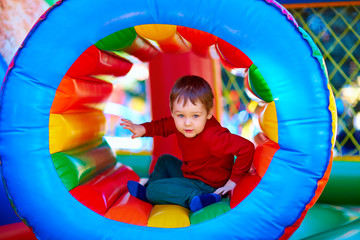 Fototapeta na wymiar cute happy kid, boy playing in inflatable attraction on playground