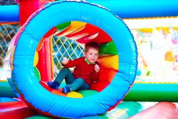 cute happy kid, boy playing in inflatable attraction on playground