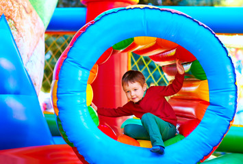 cute happy kid, boy playing in inflatable attraction on playground