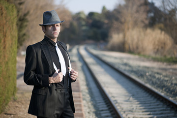 HOMBRE ELEGANTE JUNTO A LAS VIAS DEL TREN CON SOMBRERO Y MALETA