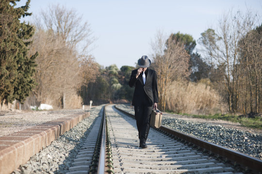 Hombre con traje y maleta antiguos camina por ra&iacute;les de tren
