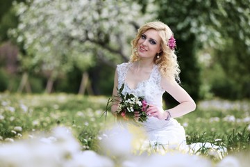 Beautiful young bride in white dress sits field in summer green park