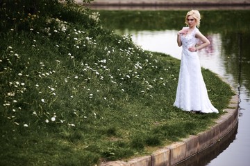 Fototapeta premium Beautiful young bride in white dress near lake in summer green park
