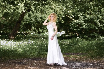 Fototapeta na wymiar Beautiful young bride in white dress in summer green park