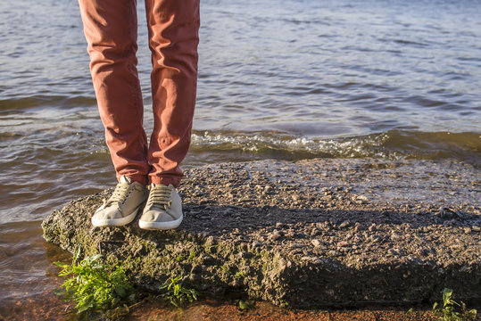 man stands on the stone by the river with small waves