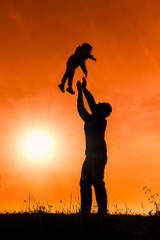 silhouette of father with baby flying over his head at orange sunset 