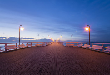 wooden pier by the sea lit by stylish lamps at night