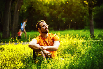 A serious thoughtful man is sitting on green grass in a park