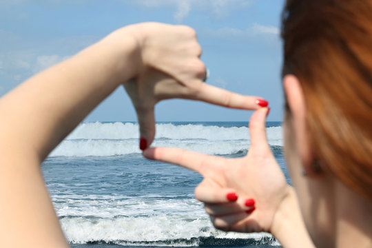 Woman hands making a frame against the blue ocean
