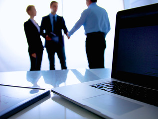 Laptop  computer on  desk , three businesspeople standing in the