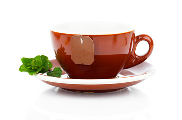 Cup of tea with tea bag and mint plant (blank label) on white ba