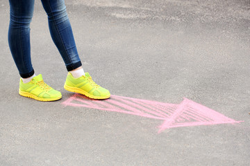Female feet and drawing arrow on pavement background
