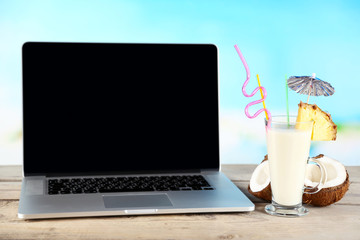 Laptop and glass of summer cocktail on wooden table, on bright blurred background - Powered by Adobe