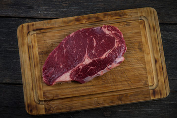 Raw ribeye beef steak overhead on wooden rustic board