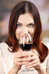 Young woman tasting wine on bright background