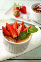 Creme brulee dessert with fresh strawberry berries on napkin, on color wooden background