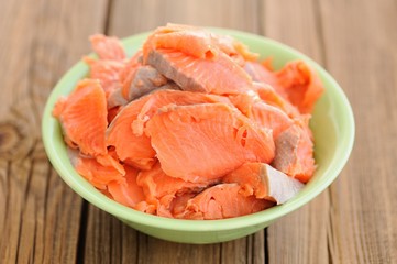 Slices of raw salmon in green bowl on wooden background